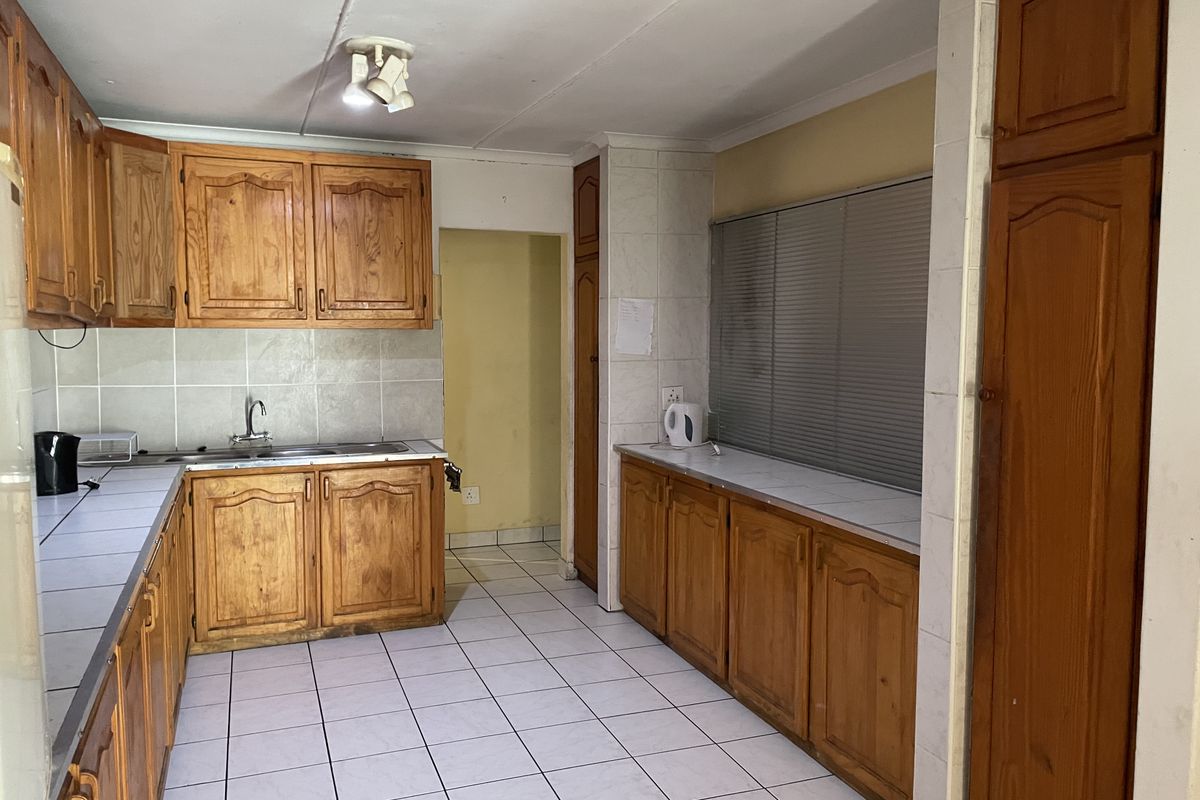 A functional kitchen featuring traditional wooden cabinetry, tiled flooring, and ample counter space, offering a solid foundation for a modern renovation.