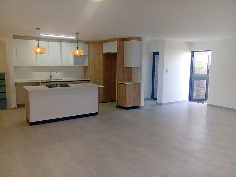 Modern open-plan living area featuring a contemporary kitchen with a central island, gas hob, and sleek cabinetry, finished with neutral floor tiles.