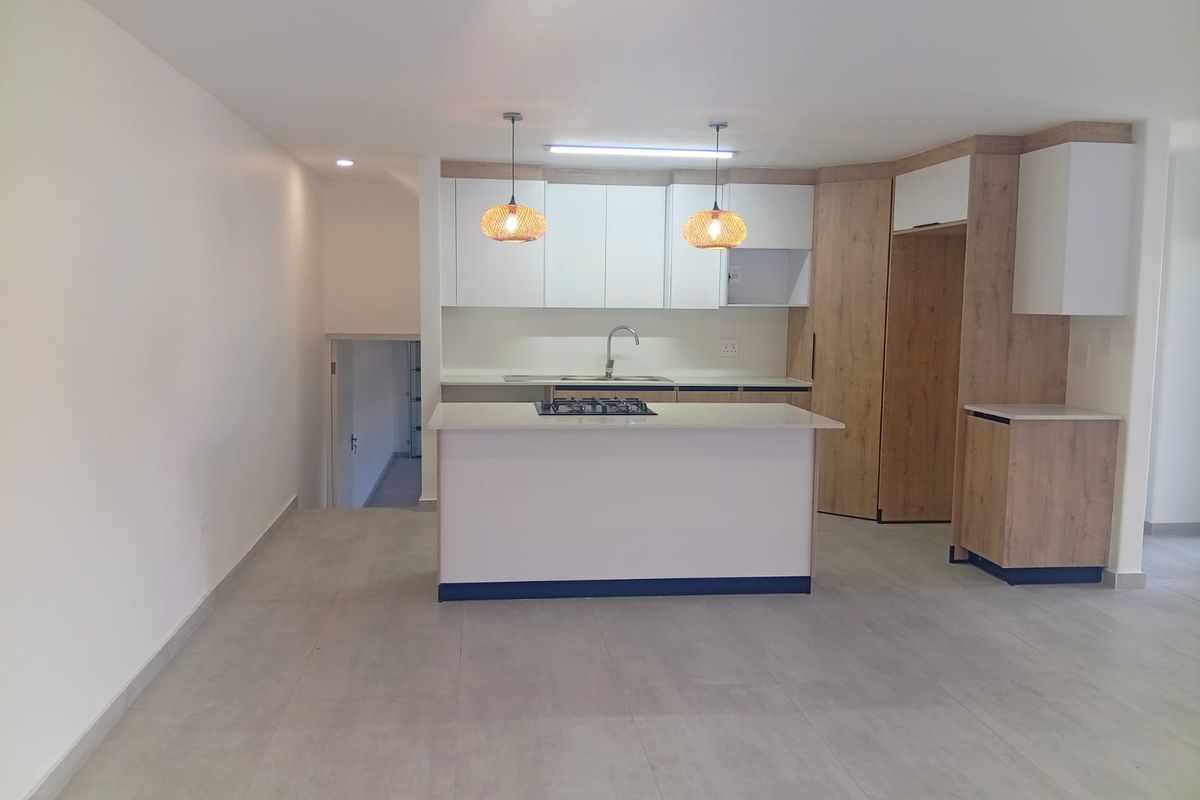 Modern kitchen featuring a central island with a gas hob, sleek cabinetry, stone countertops, and neutral tiled flooring in an open-plan layout.