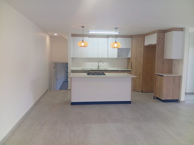 Modern kitchen featuring a central island with a gas hob, sleek cabinetry, stone countertops, and neutral tiled flooring in an open-plan layout.