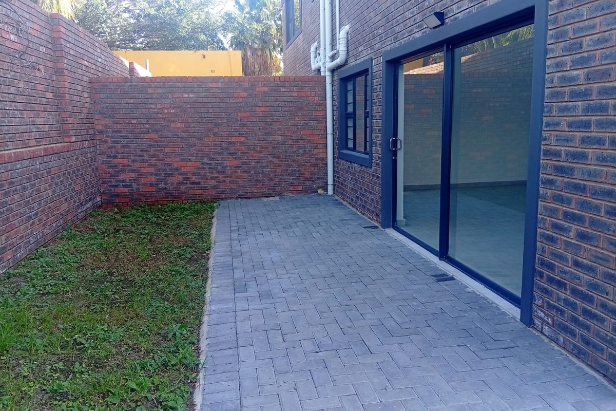 Rear exterior view of the townhouse featuring a paved patio area, brick boundary walls, and a sliding glass door entrance.