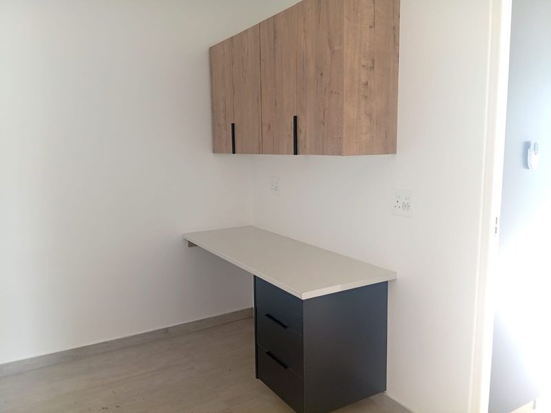 A clean, modern home office space featuring a built-in desk with under-counter storage and overhead wall-mounted cabinetry.