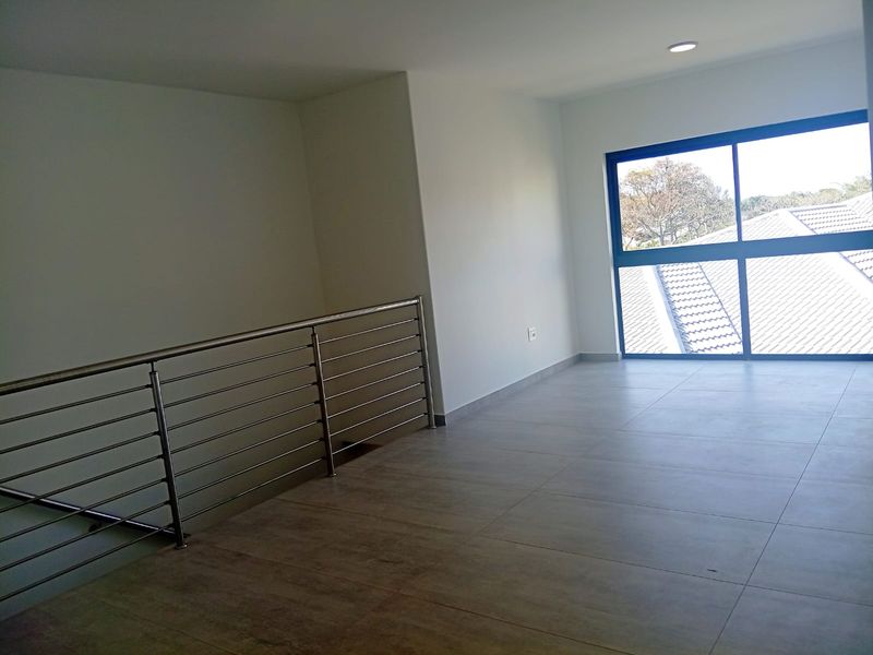 A bright, empty landing area featuring modern tiled flooring, a stainless steel balustrade, and a large window providing natural light.