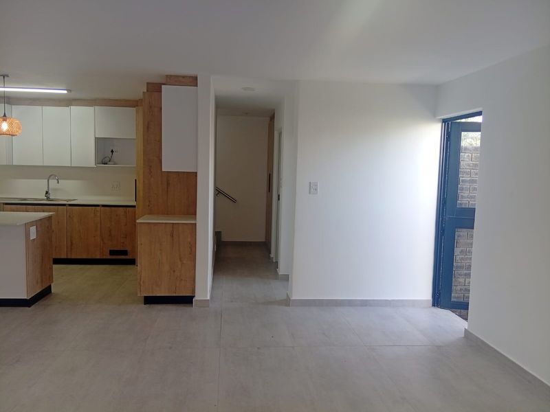 Open plan living area featuring a modern kitchen with wood-look cabinetry, a central island, and tiled flooring, leading to a staircase and exterior access.