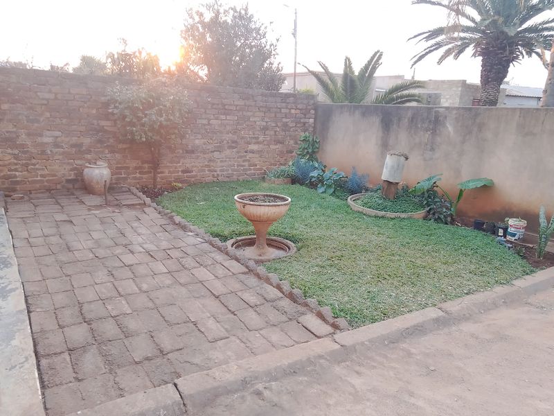 A private garden area featuring a paved patio, a small lawn, and brick boundary walls, offering a blank canvas for outdoor landscaping.