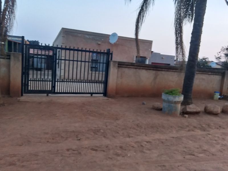 Front view of the property featuring a metal security gate, perimeter wall, and satellite dish, set against an unpaved exterior area.