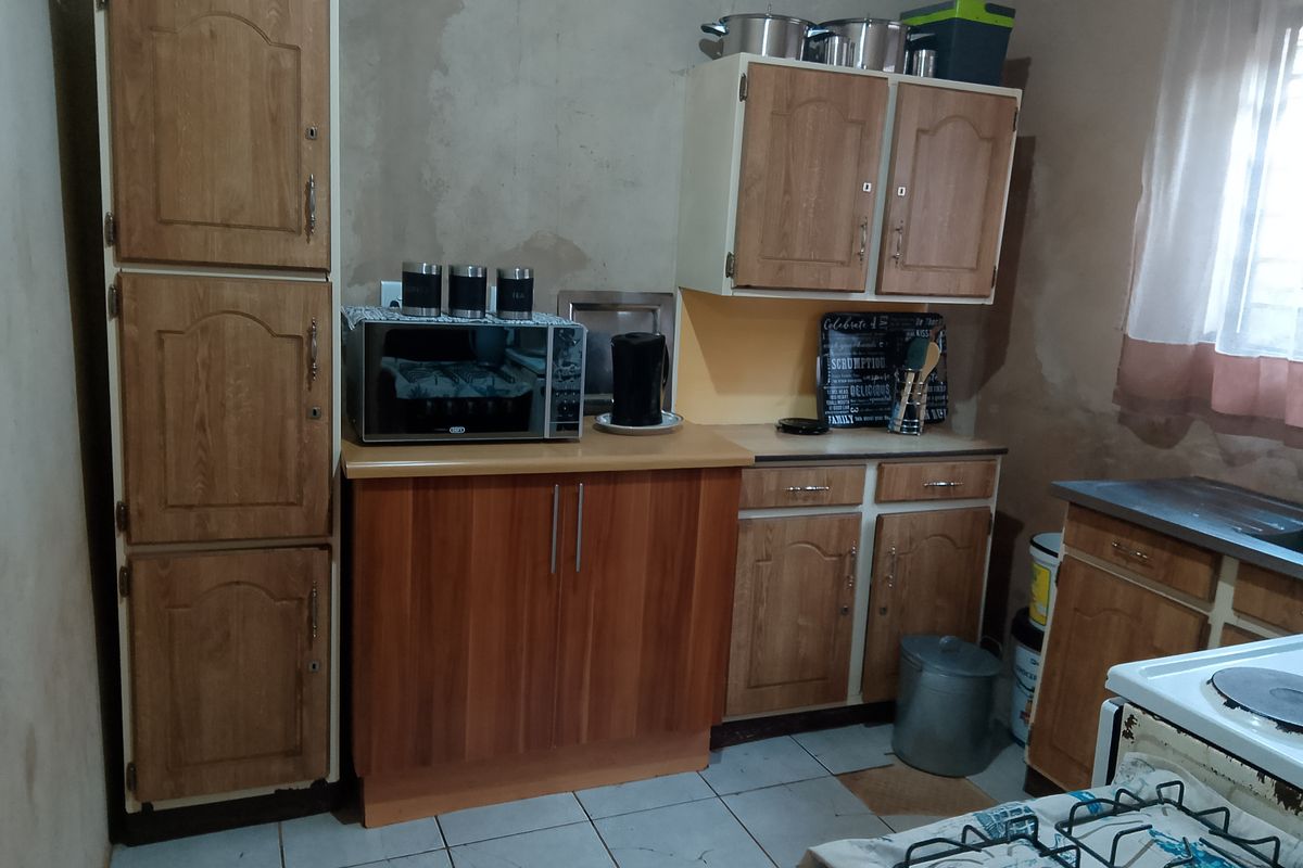 A functional kitchen featuring laminate cabinetry, tiled flooring, and a built-in stove, currently requiring wall finishing and cosmetic updates to improve the overall aesthetic.