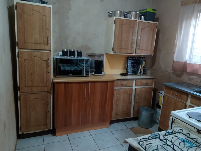 A functional kitchen featuring laminate cabinetry, tiled flooring, and a built-in stove, currently requiring wall finishing and cosmetic updates to improve the overall aesthetic.
