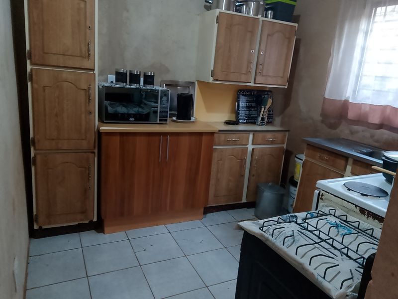A functional kitchen featuring wooden cabinetry, laminate countertops, tiled flooring, and a freestanding stove, offering potential for modernization and aesthetic updates.