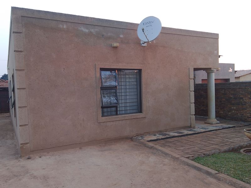 A view of the front exterior facade featuring a textured wall finish, a satellite dish, and a paved entrance area with a decorative column.