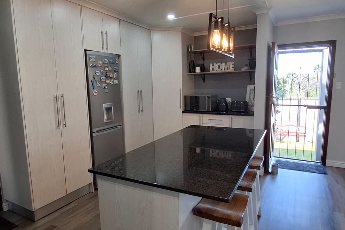Modern kitchen featuring a central island with granite countertops, ample built-in cabinetry, and stylish pendant lighting, providing a functional and contemporary cooking space.