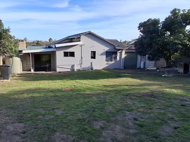 Rear view of the property featuring a spacious backyard, concrete boundary walls with security fencing, and a detached garage structure.