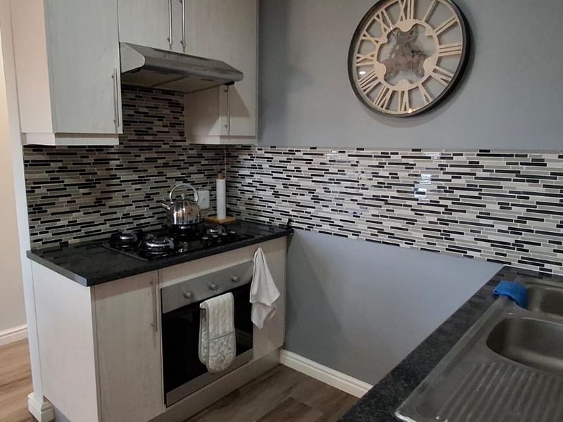 Compact kitchen featuring modern cabinetry, a gas hob with extractor fan, mosaic tile backsplash, and a double bowl stainless steel sink.