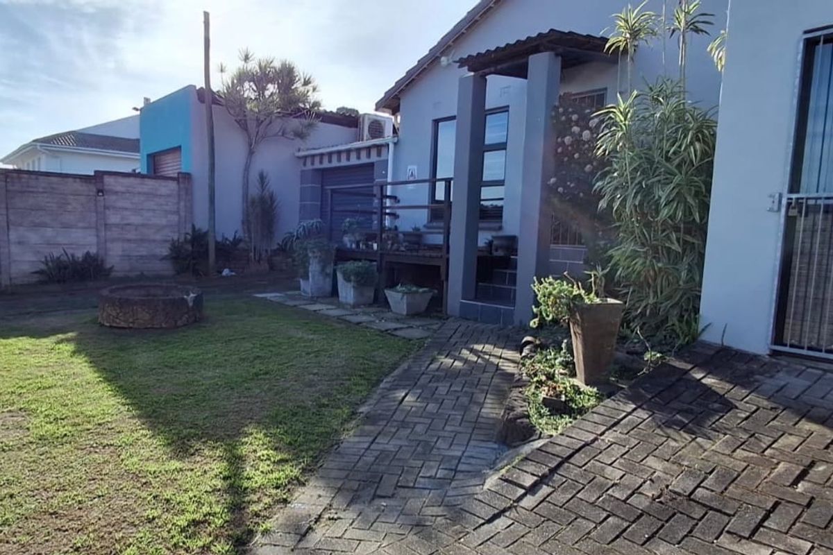 Rear garden area featuring a paved walkway, raised timber deck, stone fire pit, and secure boundary walling.