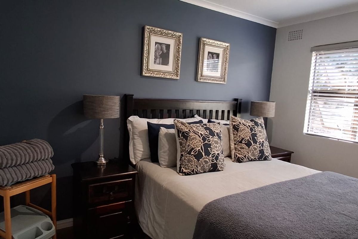 A well-maintained bedroom featuring a dark accent wall, neutral flooring, and a window fitted with venetian blinds.