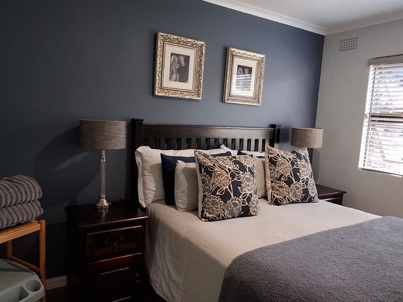A well-maintained bedroom featuring a dark accent wall, neutral flooring, and a window fitted with venetian blinds.