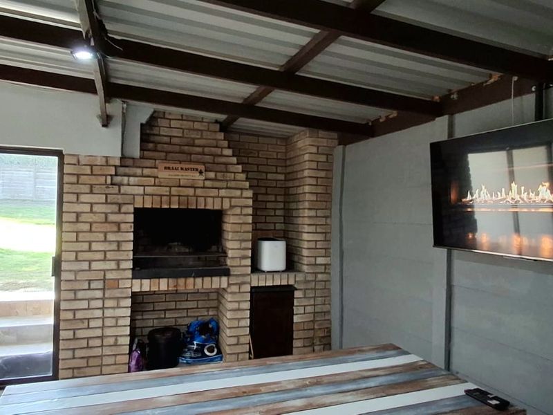 Covered outdoor patio featuring a built-in brick braai, exposed beam ceiling, and sliding glass doors providing direct access to the garden.