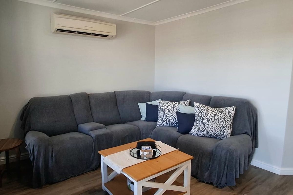 A comfortable living room featuring laminate flooring, neutral wall finishes, and a wall-mounted split-system air conditioning unit.