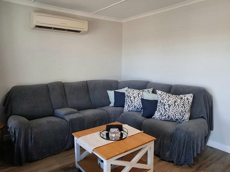 A comfortable living room featuring laminate flooring, neutral wall finishes, and a wall-mounted split-system air conditioning unit.