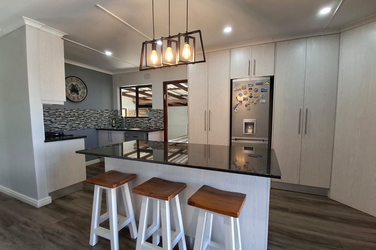Modern kitchen featuring a central island with granite countertops, light wood cabinetry, mosaic backsplash, and integrated appliances in a well-lit open space.