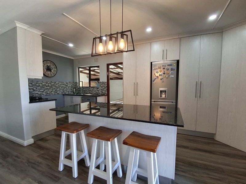 Modern kitchen featuring a central island with granite countertops, light wood cabinetry, mosaic backsplash, and integrated appliances in a well-lit open space.