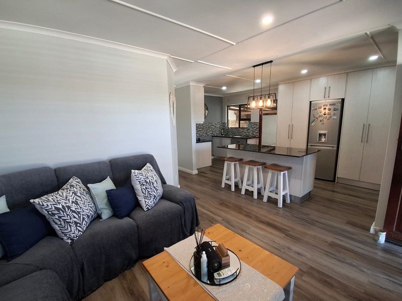 An open-plan living and kitchen area featuring modern cabinetry, a central island with granite countertops, and durable laminate flooring throughout.