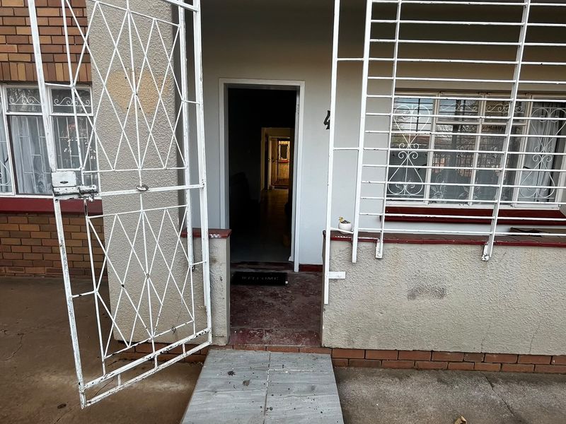Front entrance of the flat featuring a security gate, burglar bars on windows, and a tiled walkway leading to the main door.