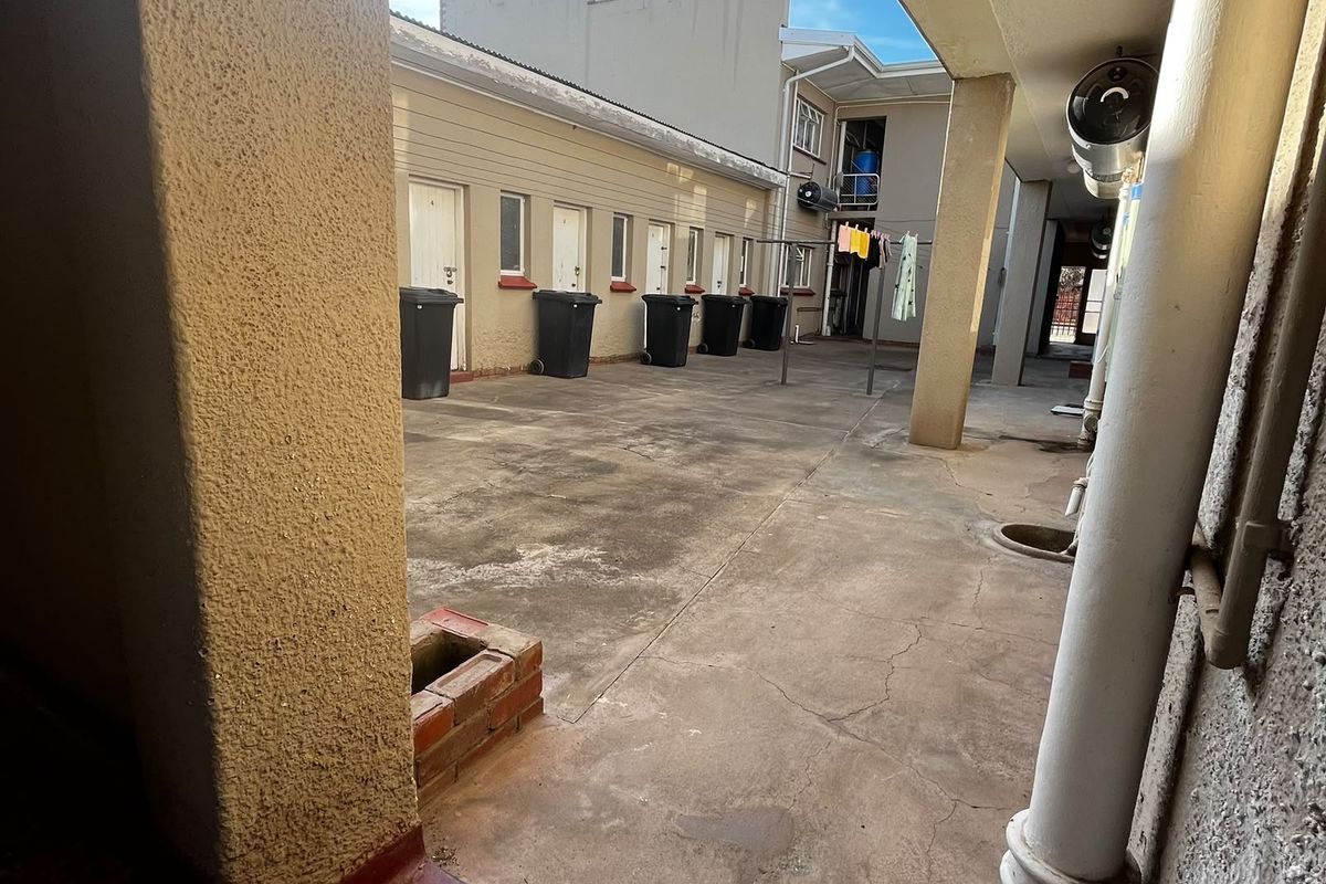 A paved rear courtyard area featuring a covered walkway, drainage infrastructure, and access to multiple unit entrances.