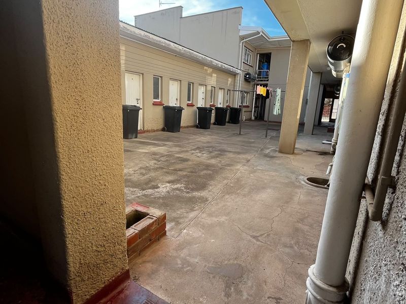 A paved rear courtyard area featuring a covered walkway, drainage infrastructure, and access to multiple unit entrances.