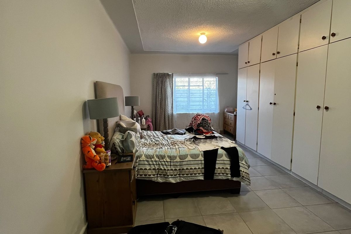 A spacious bedroom featuring extensive built-in cupboards, neutral tiled flooring, and natural light from a window.