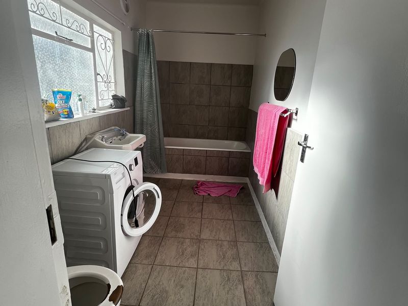 A functional bathroom featuring a bathtub, basin, and toilet, with tiled finishes and a laundry area integration.