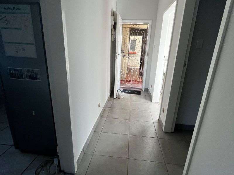 A functional hallway featuring neutral tiled flooring and a secure entrance gate, providing access to various rooms within the flat.