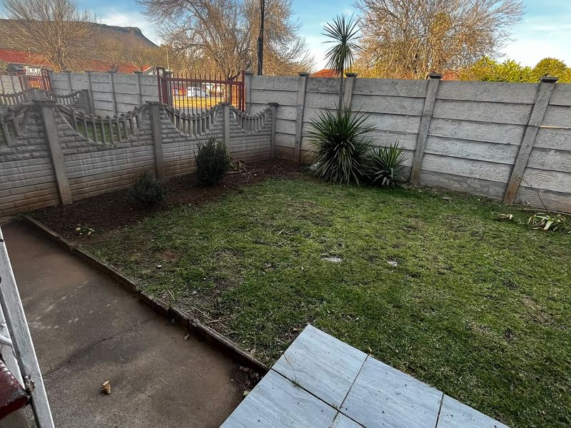 A private rear garden featuring a small lawn, concrete pathway, and a tiled patio area enclosed by precast concrete boundary walls.