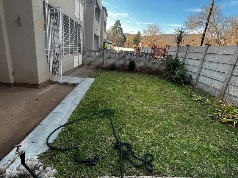 A private rear garden area featuring a lawn, paved walkway, and precast concrete boundary wall, accessible via a security gate.