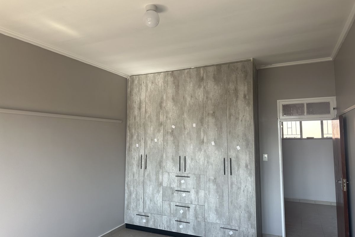 A spacious bedroom featuring modern wood-look built-in cupboards and neutral wall tones, providing a clean and functional living space.