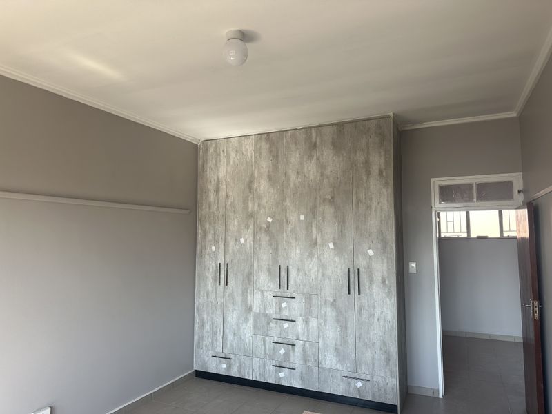A spacious bedroom featuring modern wood-look built-in cupboards and neutral wall tones, providing a clean and functional living space.