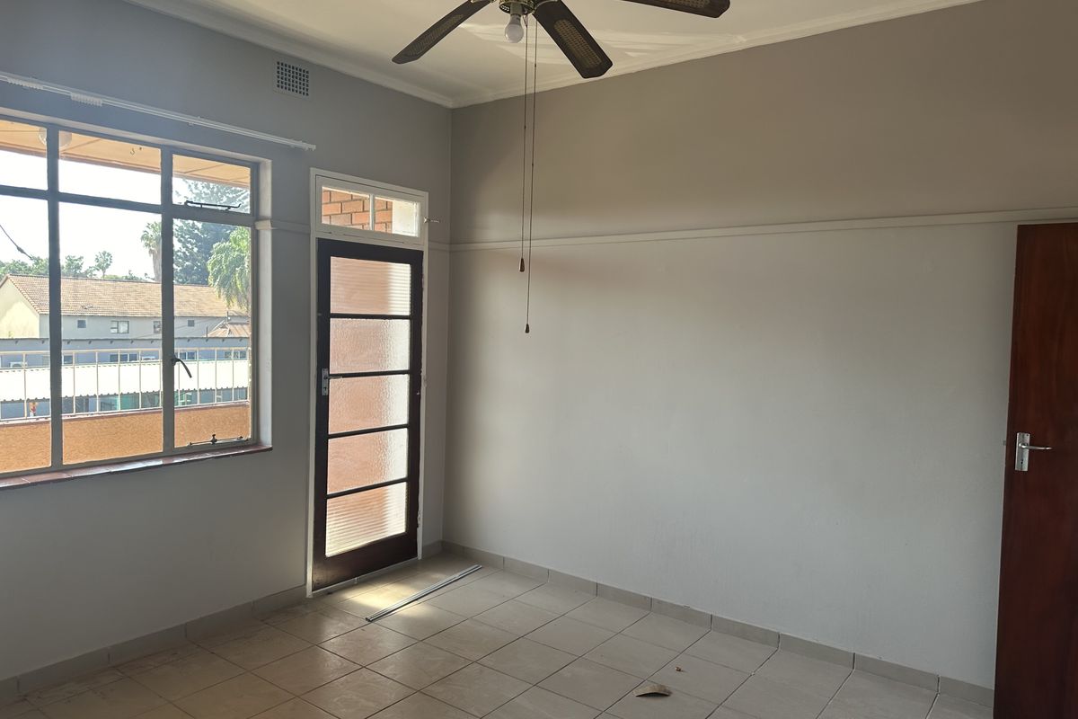 An empty living room featuring tiled flooring, a ceiling fan, and direct access to an outdoor area through a glass panel door.