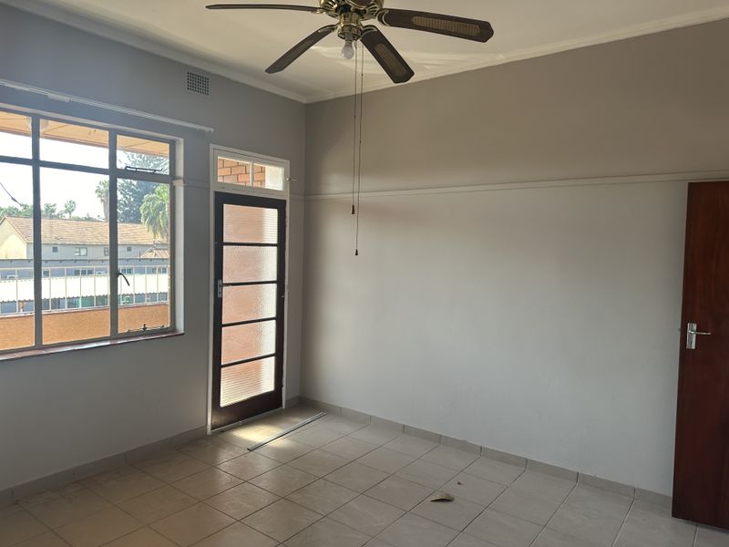 An empty living room featuring tiled flooring, a ceiling fan, and direct access to an outdoor area through a glass panel door.