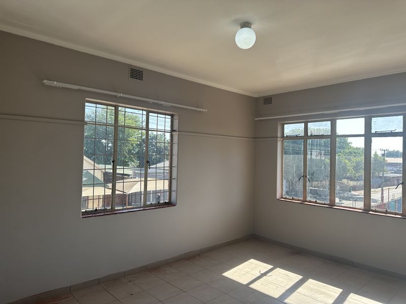An empty bedroom featuring tiled flooring, steel-framed windows with security bars, and neutral wall paint, offering a blank canvas for personalization.