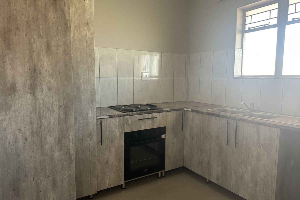 A functional kitchen featuring modern wood-look cabinetry, laminate countertops, a built-in oven and hob, and a stainless steel sink with tiled backsplash.