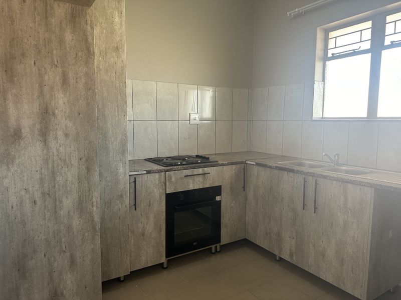 A functional kitchen featuring modern wood-look cabinetry, laminate countertops, a built-in oven and hob, and a stainless steel sink with tiled backsplash.