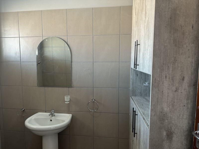 A clean bathroom featuring a pedestal basin, tiled walls, and modern built-in cabinetry for storage.