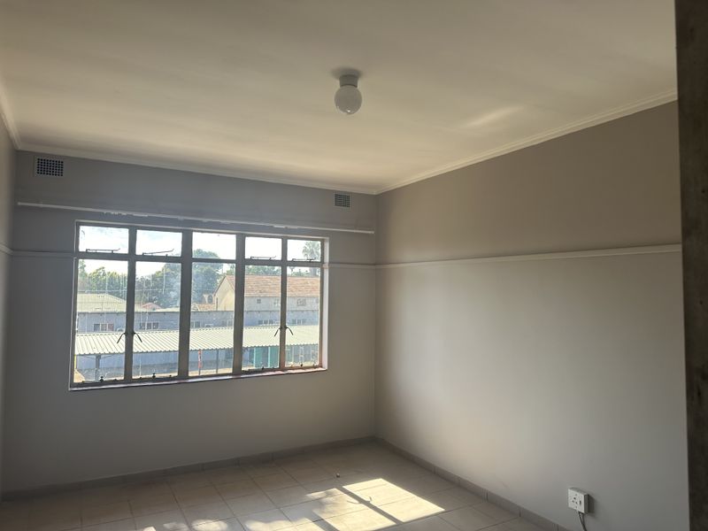A bright, empty bedroom featuring tiled flooring, a large window with natural light, and neutral wall finishes.