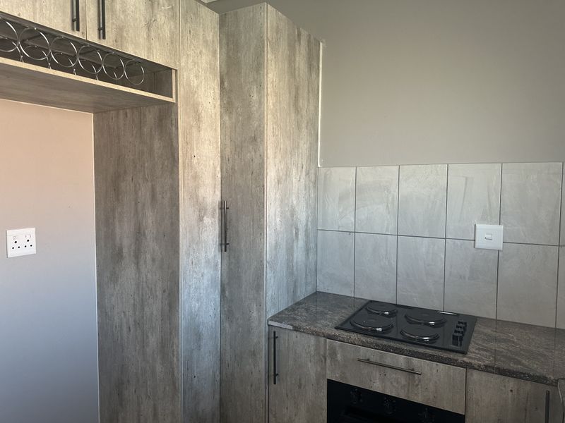 A modern kitchen featuring wood-look cabinetry, stone countertops, a built-in electric hob, and an integrated oven with a tiled splashback.