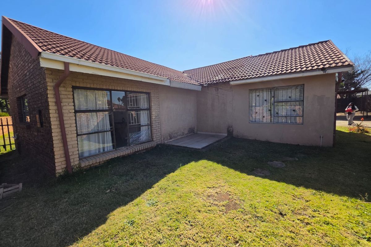 Rear view of the house featuring a tiled roof, brick and plastered exterior walls, security bars on windows, and a small paved patio area.