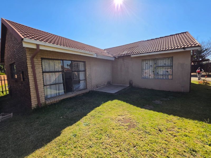 Rear view of the house featuring a tiled roof, brick and plastered exterior walls, security bars on windows, and a small paved patio area.
