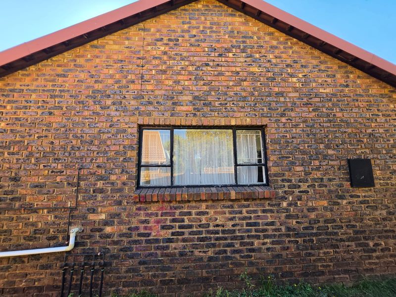 A view of the rear face brick exterior wall featuring a metal-framed window with security bars and visible external plumbing infrastructure.