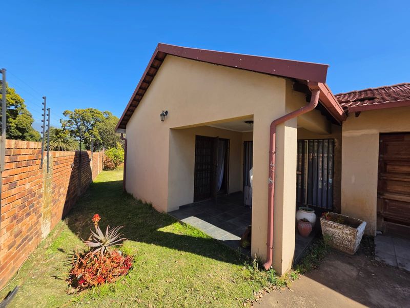A covered patio area featuring tiled flooring, adjacent to a brick boundary wall with electric fencing and established garden space.