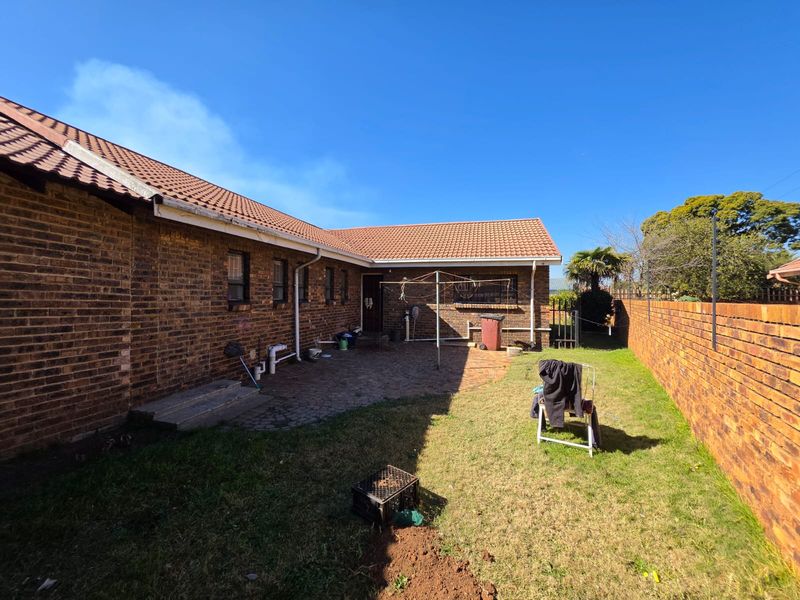 Rear view of the property featuring a brick facade, tiled roof, paved patio area, and a private garden enclosed by a brick boundary wall.