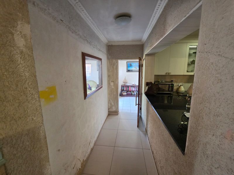 A hallway leading to an adjacent room, featuring tiled floors and a pass-through window into the kitchen with granite countertops.